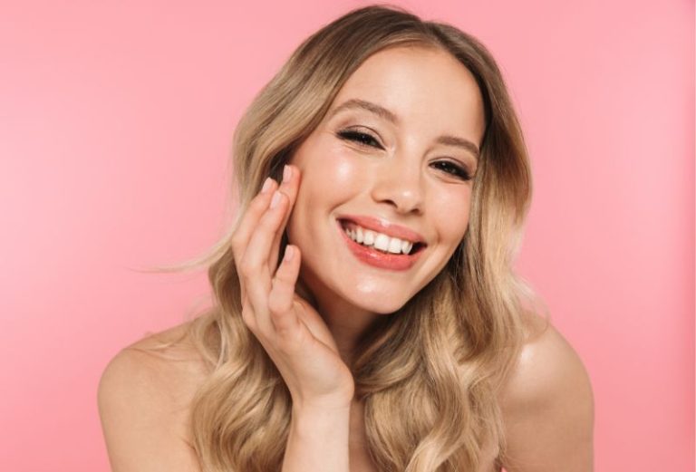 Woman looking into the camera touching her face on a pink background
