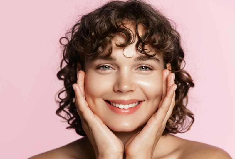 Woman with glowing skin looking into the camera holding her face